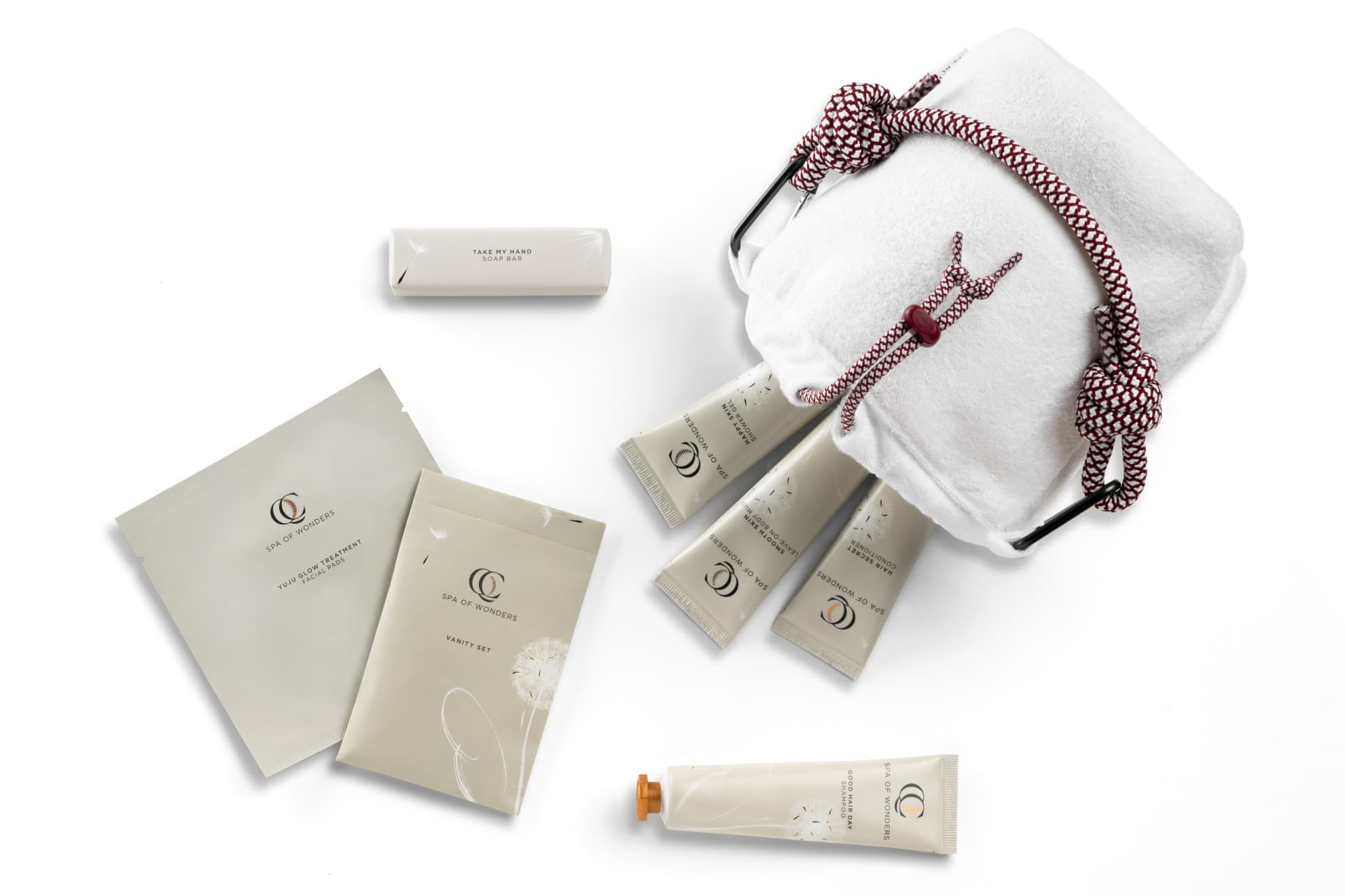 Pochette in spugna con 7 prodotti per la cura dei capelli, del corpo e delle mani, etichette frontali visibili, sfondo neutro.