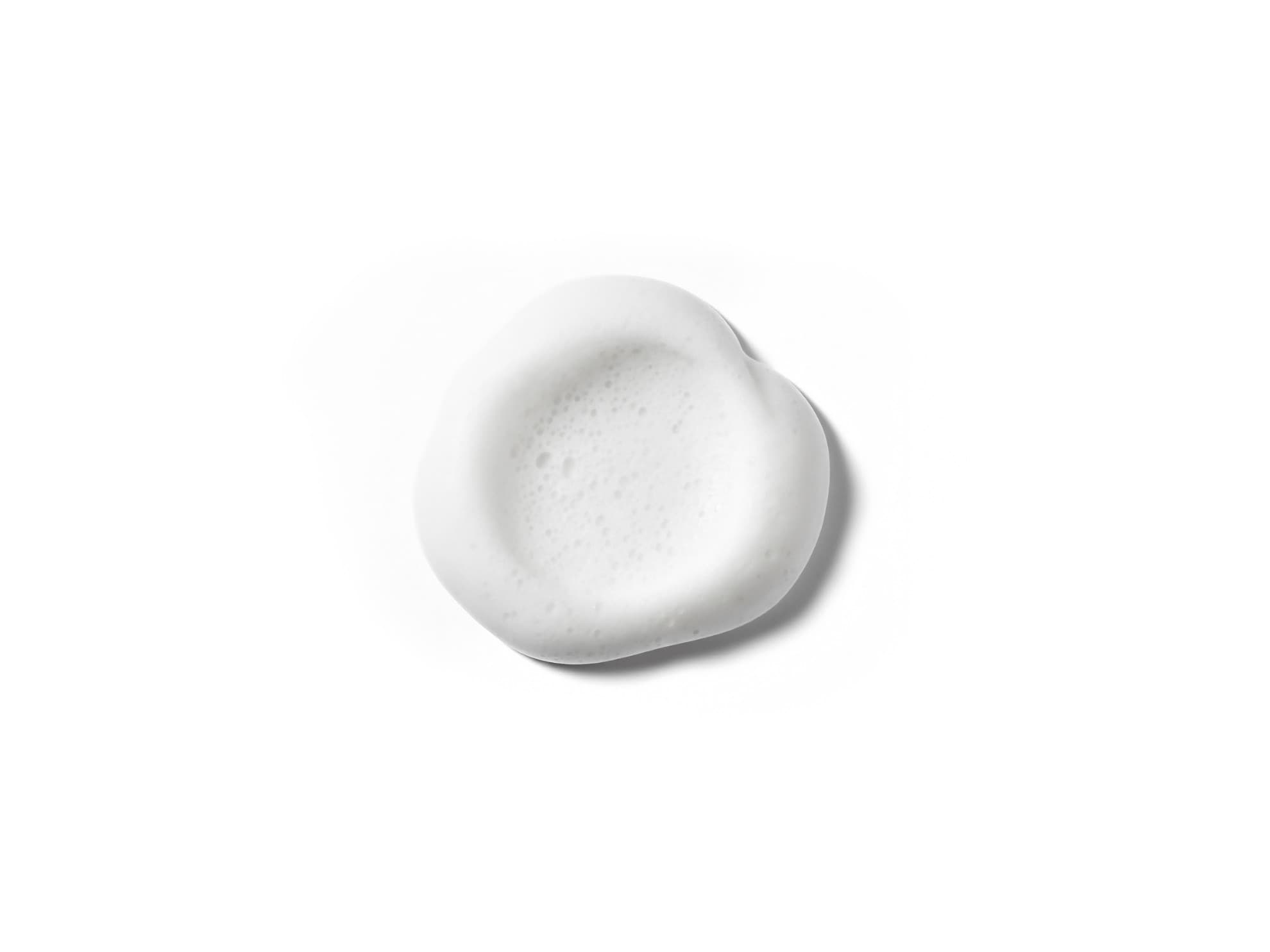 Goccia di mousse detergente idratante  su superficie bianca, texture fluida in primo piano su sfondo neutro.