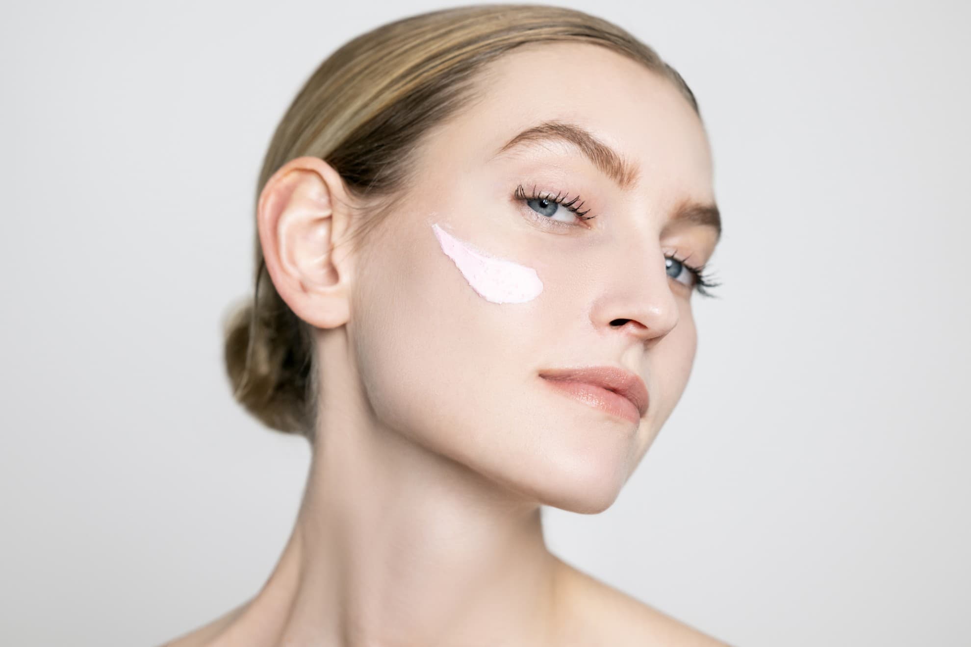 Viso di donna con maschera viso applicata sulla guancia. Viso pulito, pelle luminosa, primo piano su sfondo neutro.