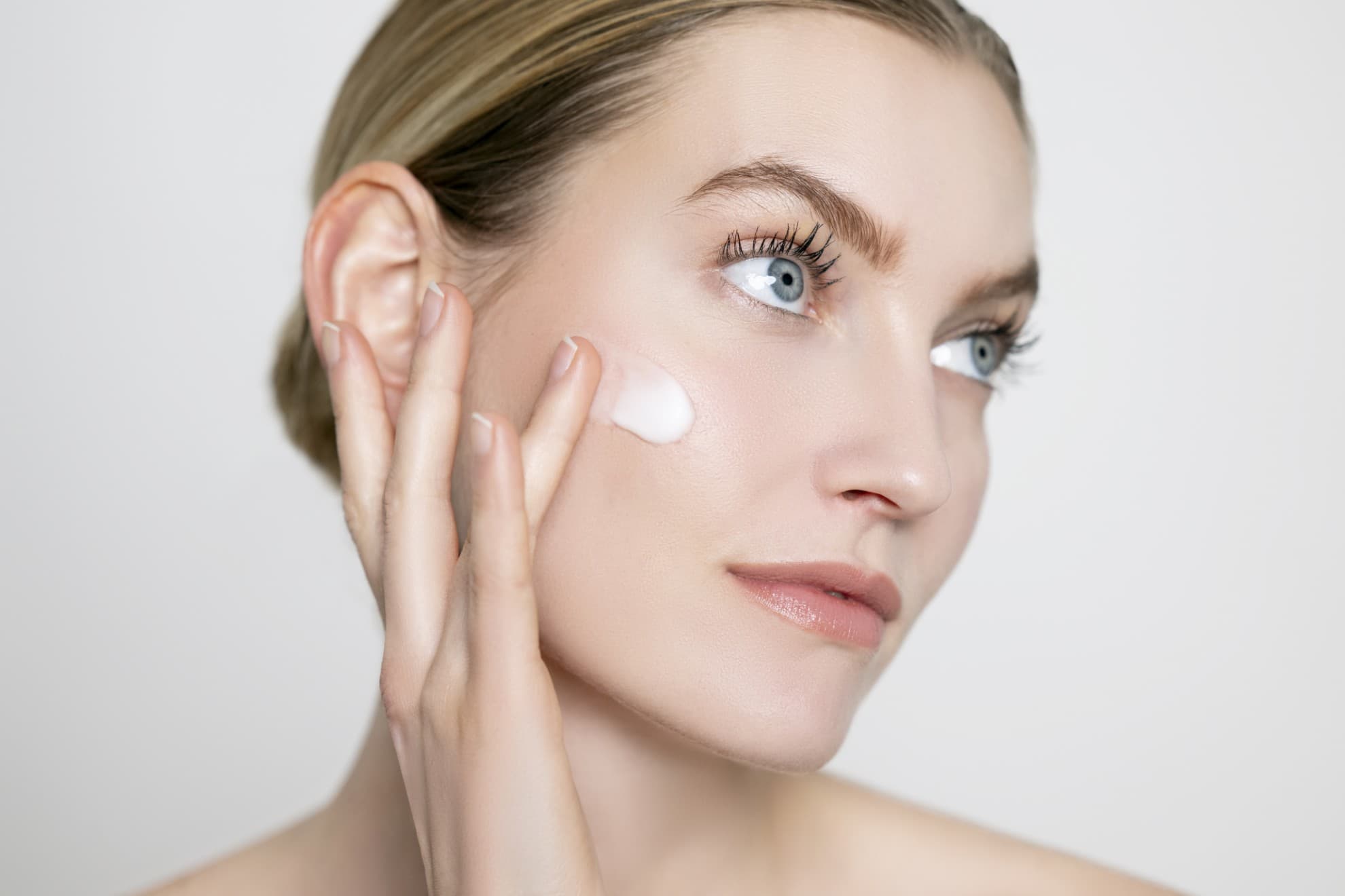 Donna applica siero viso con le dita, viso pulito, pelle luminosa, primo piano su sfondo neutro.