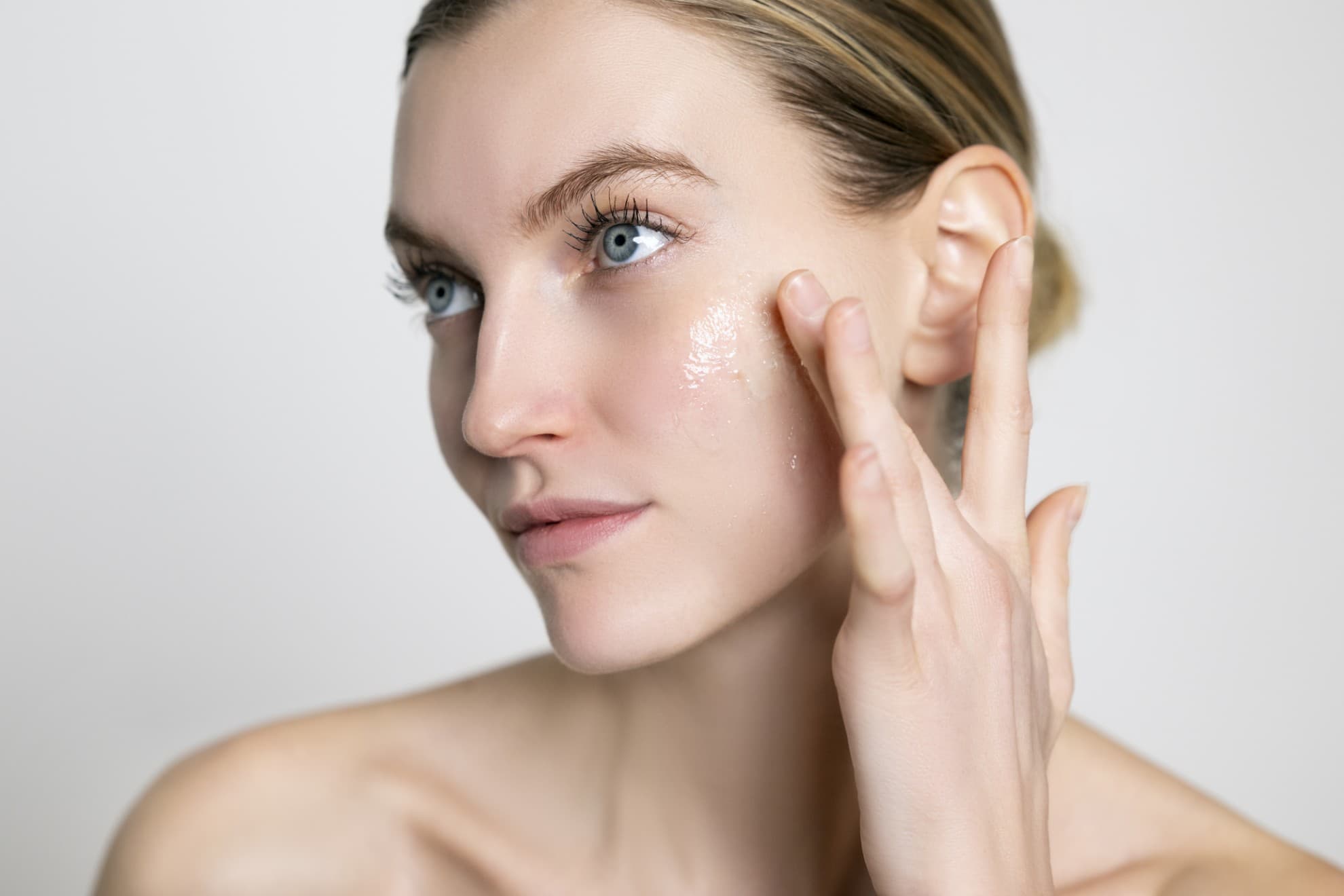 Donna applica gel micellare sul viso con le dita, viso pulito, pelle luminosa, primo piano su sfondo neutro.