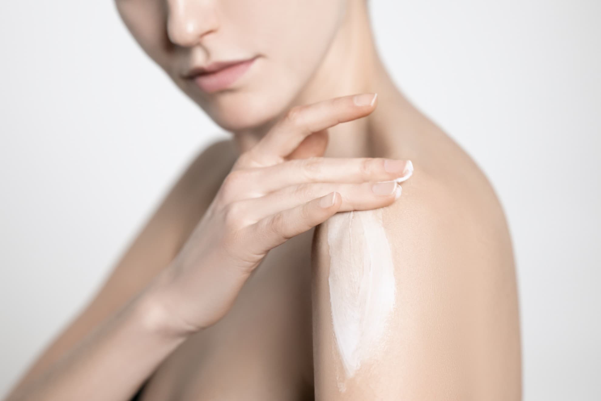 Donna applica la crema corpo velvet touch sul braccio, pelle luminosa, primo piano su sfondo neutro.