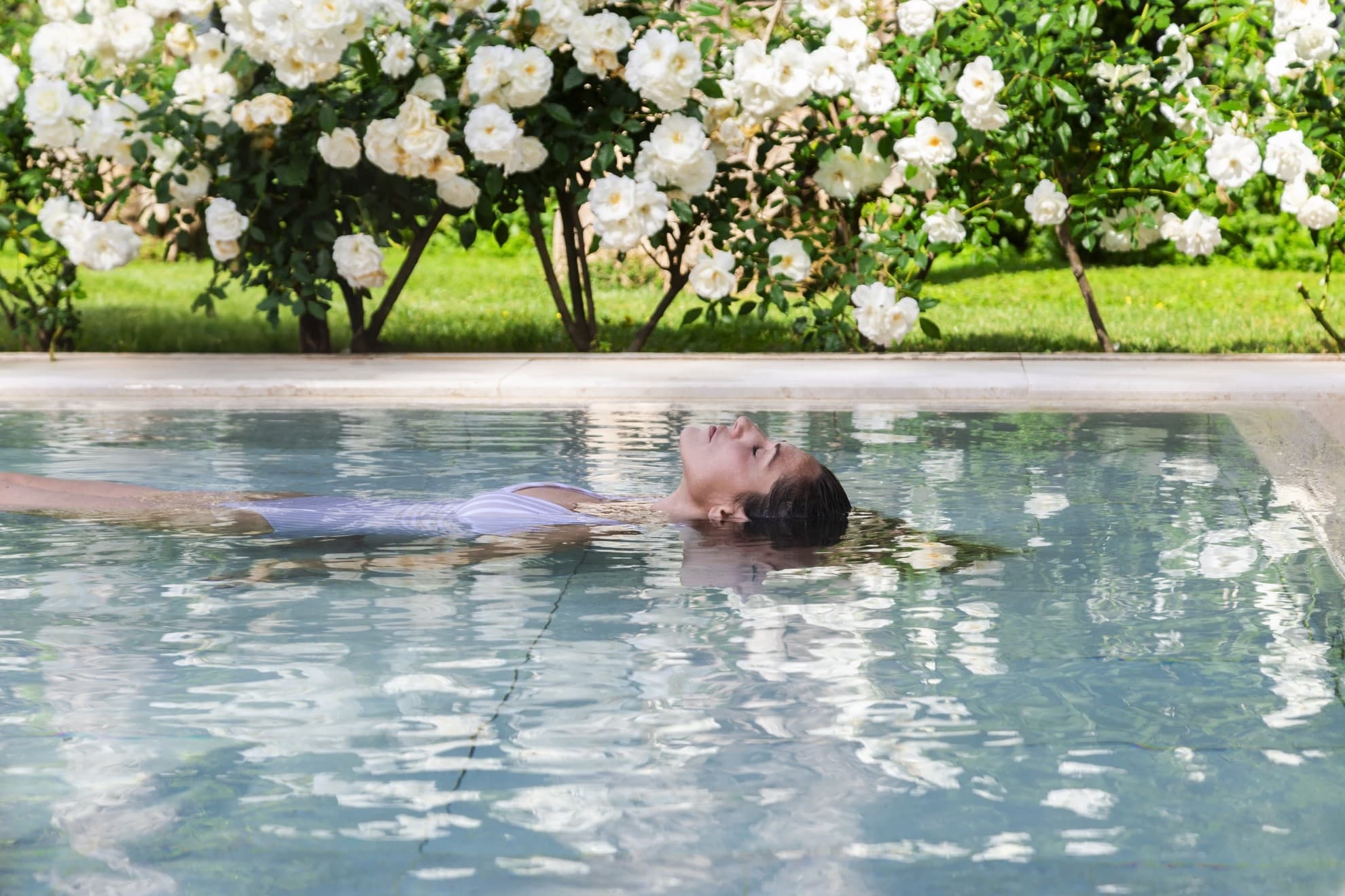 Donna sdraiata in vasca circondata da fiori bianchi.